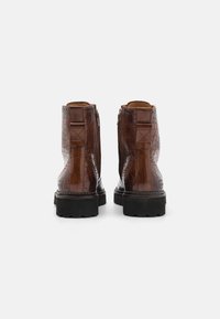 Bottines en cuir embossé crocodile marron avec une finition texturée, semelle en caoutchouc noir robuste et languettes de tirage décoratives à l'arrière.