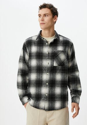 Sort-hvid plaid flannel skjorte med lange ærmer, knaplukning foran og brystlomme. Blød tekstur; afslappet pasform. Lys baggrund.