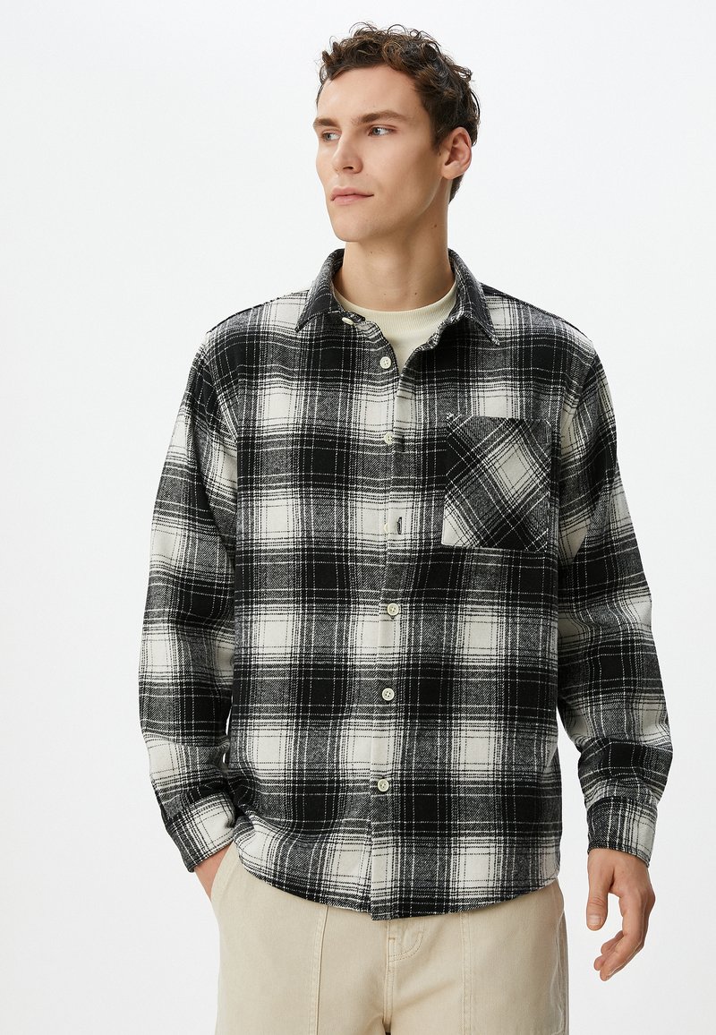 Sort-hvid plaid flannel skjorte med lange ærmer, knaplukning foran og brystlomme. Blød tekstur; afslappet pasform. Lys baggrund.
