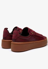 Sneakers bordeaux con una tomaia in pelle liscia e scamosciata testurizzata, occhielli dorati e una spessa suola in gomma marrone con un motivo di battistrada.