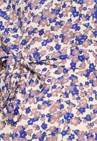 Tecido floral em creme claro com flores roxas, azuis e amarelas. Detalhe de laço na cintura, superfície texturizada e material suave e leve.