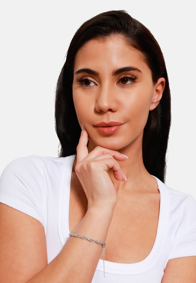 Bracciale in argento con un design delicato, caratterizzato da anelli intrecciati e un piccolo pendente, indossato su una mano su uno sfondo bianco.