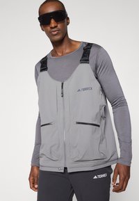Gray Terrex vest with zippered pockets, adjustable straps, and a lightweight texture; worn over a gray long-sleeve shirt.