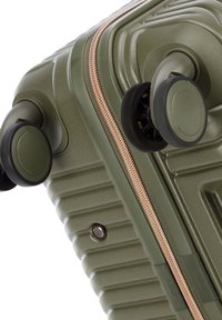 Valigia rigida verde con texture a righe, zip bronzo e doppie ruote per la mobilità. Presenta accenti circolari e una maniglia robusta.