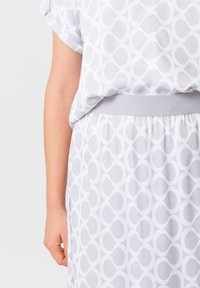 Witte jurk met een geometrisch cirkelpatroon in een iets donkere tint, met een zachte textuur en een elastische tailleband voor comfort.