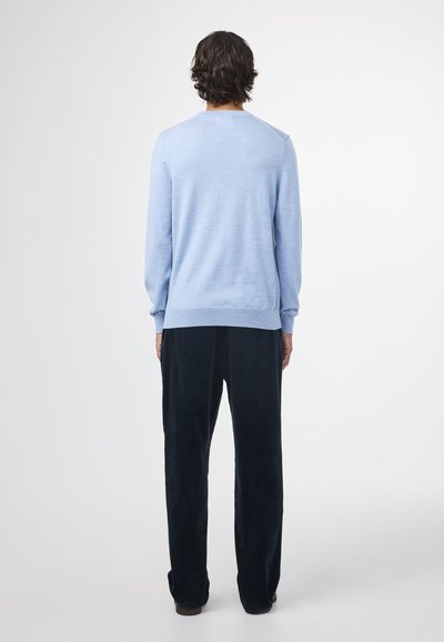 Light blue sweater in soft fabric, featuring long sleeves and ribbed cuffs, paired with dark, wide-leg corduroy pants.