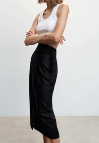 Gonna nera avvolgente con un profondo spacco, tessuto testurizzato e vita strutturata, abbinata a una canotta bianca aderente.