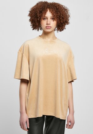 Bežové oversized tričko z mäkkého materiálu, s okrúhlym výstrihom, krátkymi rukávmi a predným logom s jemnou textúrou vzoru.