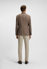 Brun rutiga kavaj med rak skärning, i kombination med ljusa beige byxor, sedd bakifrån. Slätt tyg och minimalistisk design.