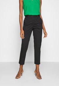 Czarne, dopasowane spodnie o wąskim kroju, z gładką fakturą, bocznymi kieszeniami oraz skróconą długością, zestawione z zieloną bluzką i sandałami na paski.