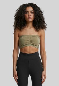 Olivovo zelený crop top bez ramienok s predným riasením a elastickým materiálom. Skombinovaný s čiernymi legínami s vysokým pásom pre priliehavý vzhľad.