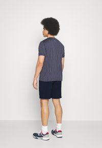 Marine stripete skjorte med korte ermer og hvite vertikale striper, kombinert med mørke shorts, hvite og marineblå joggesko, sett fra baksiden.