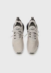 Beige sportcipők texturált hálós felsőrésszel, fekete kiegészítőkkel, lekerekített orral és fűzős záródással. Hátsó fogantyúval rendelkezik a könnyű felhúzáshoz.