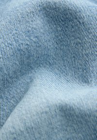 Približen posnetek svetlo modrega jeansa, ki prikazuje diagonalno tkanje in subtilne gube.