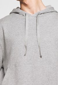 Sudadera gris hecha de tejido suave, con capucha ajustable, bolsillo tipo canguro y una silueta relajada con puños y dobladillo acanalados.