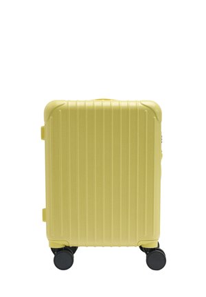 Mała bladożółta twarda walizka z pionowymi rowkami, ochraniaczami na narożnikach i czterema czarnymi obrotowymi kółkami.