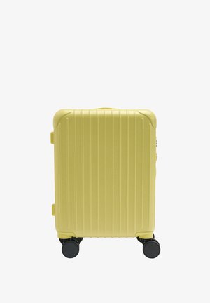 Mała bladożółta twarda walizka z pionowymi rowkami, ochraniaczami na narożnikach i czterema czarnymi obrotowymi kółkami.