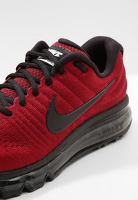 Červená sportovní obuv s texturovaným svrškem, černé logo Nike swoosh a černé tkaničky. Obsahuje viditelnou vzduchovou výplň podrážky pro větší pohodlí.