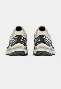 Μπεζ και μαύρα παπούτσια για τρέξιμο σε μονοπάτια με υφή στο επάνω μέρος, επενδεδυμένη στήριξη αστραγάλου και καλοσχηματισμένη λαστιχένια σόλα με πέλματα.