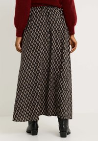 Jupe noire fluide avec un motif floral en losange crème et or. Présente une taille froncée et une silhouette légèrement évasée, portée avec des bottes noires.