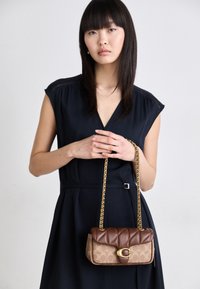 Brown quilted handbag with a gold chain strap, featuring a monogram pattern and a gold-tone logo accent on the front.