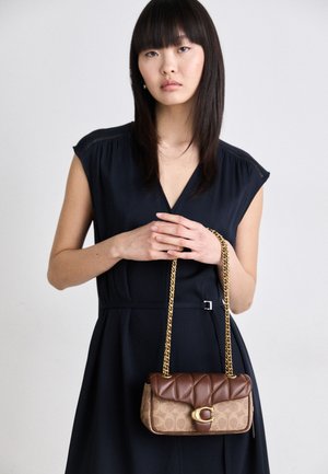 Brązowa pikowana torebka z złotym łańcuchem, z wzorem monogramu i złotym logo na froncie.