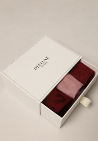 Ensemble de trois paires de chaussettes dans une boîte blanche. Comprend une paire rouge foncé, une paire rose clair et une paire bordeaux à motifs avec des accents brillants. La boîte dispose d'un onglet de traction.