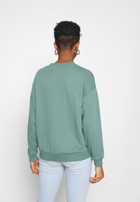 Mintgrön sweatshirt med avslappnad passform, ribbade ärmslut och nederkant samt rund halsringning, ihop med ljusblå jeans. Slät textur, avslappnad design.
