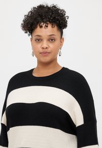 Svart og kremstripet strikkegenser med vid halsutringning og teksturert stoff. Har ribbestrikkede detaljer langs kanten og ermene.