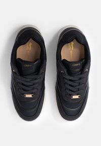 Black sneakers with smooth leather upper, contrasting suede accents, lace-up design, and a white rubber outsole. Gold branding on tongue.