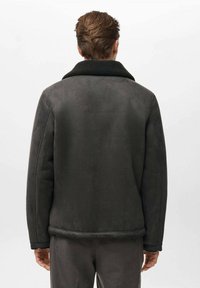 Giacca in shearling grigio scuro con colletto nero. Presenta una texture liscia, una vestibilità sartoriale e punti di cucitura sottili sui bordi.