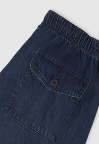 Σκούρο μπλε τζιν παντελόνι με ελαστική μέση, με τετράγωνη πίσω τσέπη και λεπτομέρεια με μαύρο κουμπί. Ομαλή υφή.