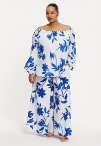 Witte outfit met een blauw bloemmotief, bestaande uit een off-the-shoulder top en wijde broekspijpen, gemaakt van lichtgewicht stof met eigenwijze mouwen.