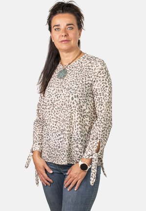 Blusa con estampado de leopardo en una tela ligera y texturizada. Presenta mangas largas con detalles de lazo y un cuello redondo. Llevada con vaqueros.