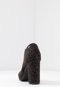 Lodička na vysokém podpatku s černou leopardí potaženou látkou, zaoblenou špičkou a masivním podpatkem. Obsahuje malý kovový akcent poblíž paty.