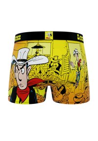 Un caleçon en tissu extensible présente un dégradé de jaune avec des illustrations de style bande dessinée représentant des cow-boys et un personnage portant un chapeau blanc.