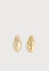 Ein Paar glänzende, glatte, unregelmäßig ovale goldene Ohrstecker, die auf einer schlichten, hellen Oberfläche liegen.