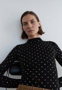 Czarna bluzka z długim rękawem i wysokim kołnierzem, z metalicznymi srebrnymi i złotymi wzorami kropek; dopasowany fason z miękkiej tekstury.