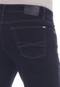Jeans de mezclilla negros con una etiqueta de cuero en la cintura y costuras en blanco contrastantes en los detalles de los bolsillos y las costuras.