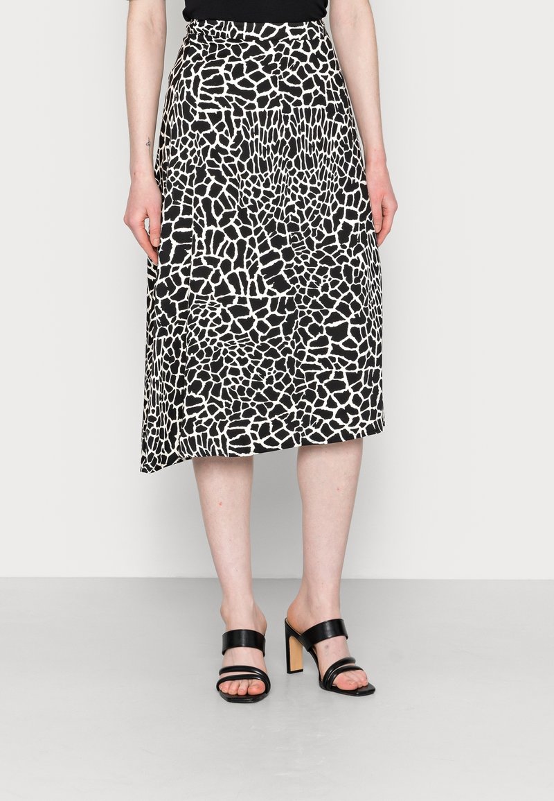 Schwarz-weißer Midi-Rock mit giraffenähnlichem Muster, fließendem Design und hoher Taille, kombiniert mit schwarzen Absatzsandalen.