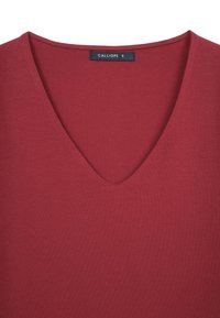 T-shirt bordeaux a V realizzato in tessuto morbido, caratterizzato da una superficie liscia e senza motivi. Include un'etichetta con "CALLIOPE S".