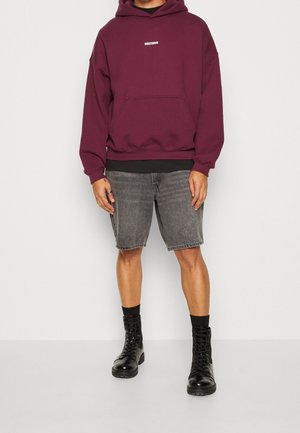 Maroon hoodie with a front pocket, black accents, gray denim shorts, and black lace-up boots. Casual, relaxed fit with visible stitching.