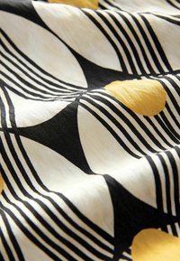 Tissu présentant un motif noir et blanc avec des formes courbes et des accents jaunes en pois. Le tissu a une texture lisse, disposé en plis.