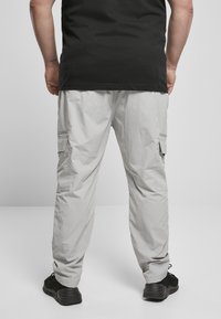 Hellgraue Cargo-Hose mit entspannter Passform, elastischem Bund, seitlichen Taschen und strukturiertem Stoff. Schwarze Schuhe sind am unteren Rand sichtbar.