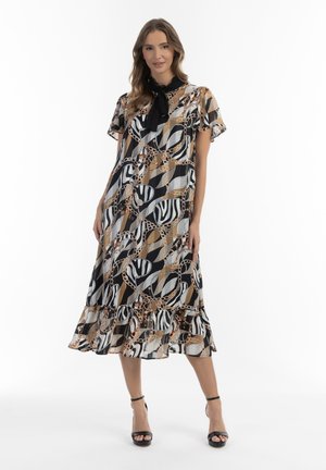 Zwart, beige en wit gemêleerde midi-jurk met korte mouwen, een strikhalslijn en een gerimpelde zoom met abstracte vormen en kettingen.