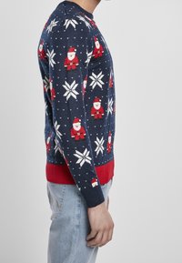 Pull de Noël bleu marine avec des motifs de Santa Claus et de flocons de neige, tricoté avec des accents rouges aux poignets et à l'ourlet.