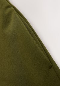 Close-up of an olive green textured fabric with visible seams and stitching details.