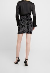 Svart satinblus med lång ärm, kombinerad med en svart sammet mini kjol som har intrikata silverblommönster, och svarta högklackade sandaler.