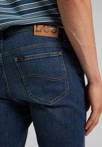 Mörkblå denimjeans med en brun läderlogotyp på baksidan, synlig sömnad och en standard design för bakfickan.