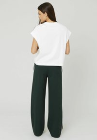 Haut blanc à manches courtes associé à un pantalon large vert foncé avec des bandes latérales. Le tissu semble doux avec une coupe décontractée.
